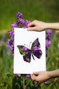 Holding papercut miniature butterfly over blooming flowers