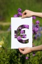 Holding papercut miniature euro over blooming flowers