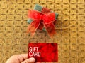 Holding a red gift card with a green gift box with big red ribbon with golden background.