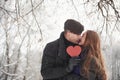 Holding red heart shaped cardboard. Gorgeous young couple have good time together in snowy forest Royalty Free Stock Photo