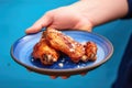 holding a saucy chicken wing over a blue plate