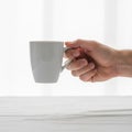 Is holding a simple, white ceramic mug with a handle, set against a Royalty Free Stock Photo