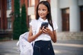Holding smartphone. School girl in uniform is outdoors near the building