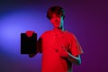 Holding tablet, crazy excited. Caucasian young man& x27;s portrait on black studio background in neon light. Beautiful male Royalty Free Stock Photo