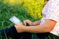 Holding tablet outside. Young woman using tablet outdoor outside. Green grass in park on sunny summer day sitting on Royalty Free Stock Photo