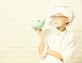 Holding turquoise bowl with chocolate cookies on brick wall background,copy space. stained cute cook chef boy