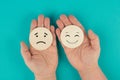 Holding two wooden circles in the hands one face is sad the other one is smiling, porsitive negative