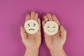 Holding two wooden circles in the hands one face is sad the other one is smiling, porsitive negative