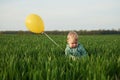 Holding yellow balloon. Cute little baby boy is in the agricultural field at daytime Royalty Free Stock Photo