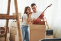 Holds acoustic guitar in hands. Cheerful young couple in their new apartment. Conception of moving