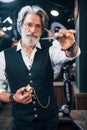 Holds barbershop equipment. Stylish modern senior man with gray hair and beard is indoors