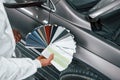 Holds cards with different colors. Caucasian automobile repairman in uniform works in garage