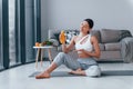 Holds glass with orange juice in hands. Young woman with slim body shape in sportswear have fitness day indoors at home Royalty Free Stock Photo