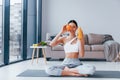 Holds glass with orange juice in hands. Young woman with slim body shape in sportswear have fitness day indoors at home Royalty Free Stock Photo