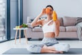 Holds glass with orange juice in hands. Young woman with slim body shape in sportswear have fitness day indoors at home Royalty Free Stock Photo