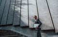 Holds laptop in hands. Young businessman in grey formal wear is outdoors in the city