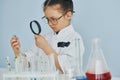 Holds magnifying glass. Little girl in coat playing a scientist in lab by using equipment