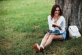 Holds pen and smiles. Young woman have weekend and sits in the park at daytime Royalty Free Stock Photo