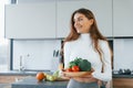 Holds plate with vegetables. Young european woman is indoors at kitchen indoors with healthy food Royalty Free Stock Photo