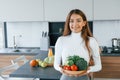 Holds plate with vegetables. Young european woman is indoors at kitchen indoors with healthy food Royalty Free Stock Photo