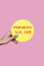 holds a sign with the text my pronouns are she, her