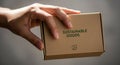 Holds a small rectangular cardboard box labeled SUSTAINABLE GOODS in Royalty Free Stock Photo