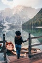 Holds on a wooden pier. Woman in black hat enjoying majestic mountain landscape near the lake with boats