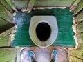 Hole of the old dirty country toilet and foots in sneakers, top view