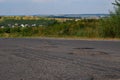 Hole in the road. Broken asphalt. Destroyed surface. Cracked road. Ukrainian landscape in the background Royalty Free Stock Photo
