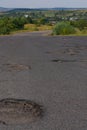 Hole in the road. Broken asphalt. Destroyed surface. Cracked road. Ukrainian landscape in the background. Royalty Free Stock Photo