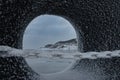 Hole in a snowy stone with mountains and a sandy beach in the background Royalty Free Stock Photo