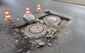 Holes and damage on an asphalt road, secured by red and white shut-off cones because of the risk of accidents