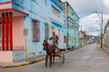 Holguin, Cuba: Local Cubans outside on a residential street. Local resident Cuban rides in a cart with a horse.