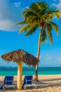 Holguin, Cuba, Playa Esmeralda. Umbrella and two lounge chairs around palm trees. Tropical beach on the Caribbean sea. Royalty Free Stock Photo