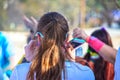 Holi Color Festival - Girl with pony tail and turquoise sunglasses and bright colored phone in hand runs through a color station