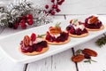 Holiday appetizers with cranberries, goat cheese and pecans on a serving plate, close up against white wood
