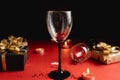 Two clinking wine glasses, various handmade gift boxes decorated with confetti, candle on red and black background.