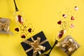 Two clinking wine glasses, various handmade gift boxes decorated with red heart confetti on yellow background.