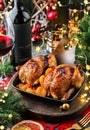 Holiday baked quail or chicken with dried apricots in pan on red napkin served with glasses, bottle of wine, candles, fir branches