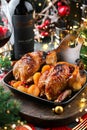 Holiday baked quail or chicken with dried apricots in pan on red napkin served with glasses, bottle of wine, candles, fir branches