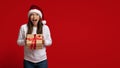 Holiday Bonus. Emotional Young Woman In Santa Hat Holding Gift Box