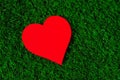 Holiday card: red paper heart lies on a green grass