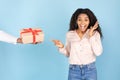 Holiday celebration concept. Male hand holding gift and giving box to surprised young woman, blue background Royalty Free Stock Photo