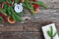 Holiday Christmas card with fir branches, Holly berries, dried oranges, gift, and alarm clock on rustic wooden Royalty Free Stock Photo