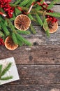 Holiday Christmas card with fir branches, Holly berries, dried oranges, gift, etc. on rustic wooden background. Royalty Free Stock Photo