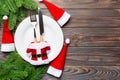 Holiday composition of plate and flatware decorated with Santa hat and clothes on wooden background. Top view of Christmas Royalty Free Stock Photo