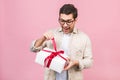 Holiday concept. Portrait of a young man opening gift box isolated over pink background Royalty Free Stock Photo