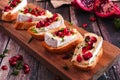 Holiday crostini appetizers with brie cheese, pomegranates and parsley, close up on a serving board against rustic wood