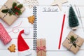 Holiday decorations, gift, present box, miniature fir tree and notebook with christmato do list on white wooden table from above.