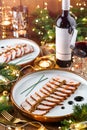 Holiday dish of sliced baked meat with sauce in plate on wooden table served with plate, glasses, bottle of wine, candles, fir